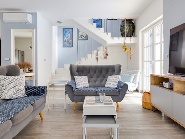 A modern living room with a grey sofa, a white coffee table, and a staircase leading to an upper level.