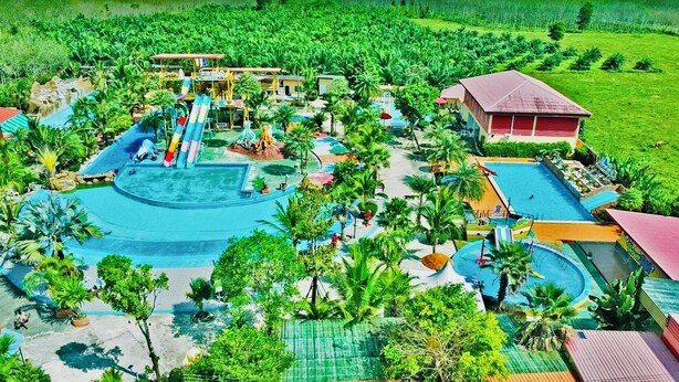 Un resort con una piscina grande, toboganes acuáticos, palmeras y un edificio rojo.