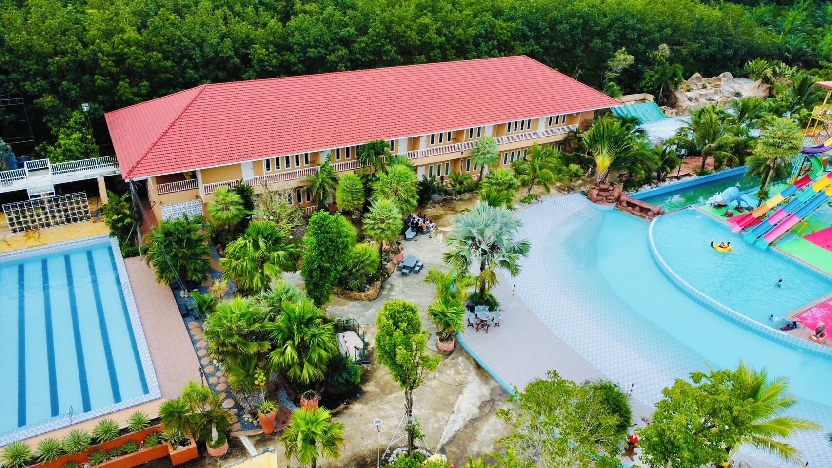 Un resort con piscina, zona de piscinas separada y un edificio de techo rojo.