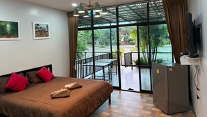 Habitación de hotel con cama, televisor, refrigerador y balcón con vista a zonas verdes.