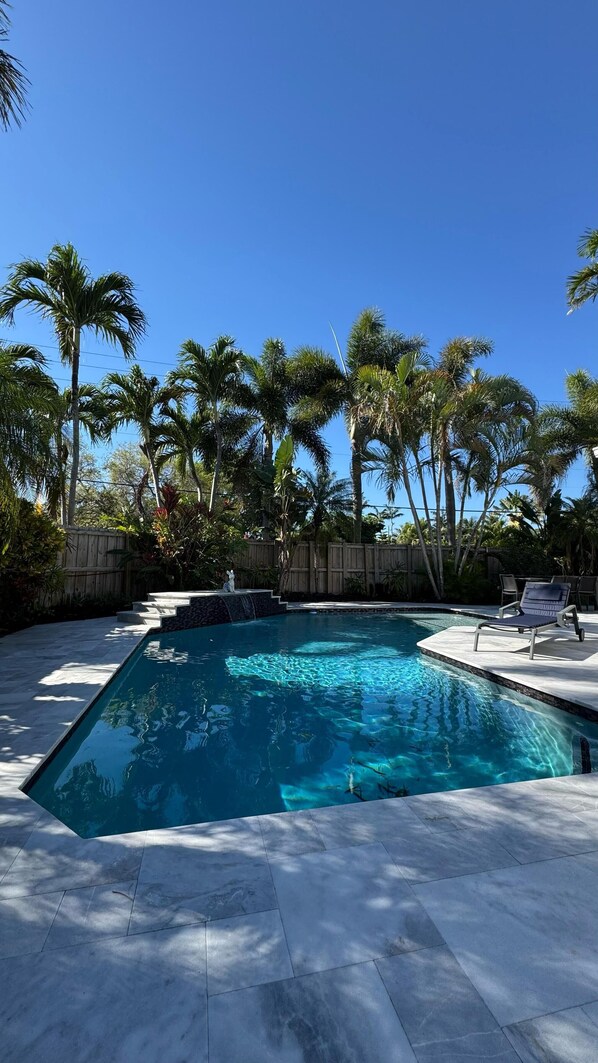 Piscina rectangular con agua azul cristalina, rodeada por una valla de madera y palmeras.