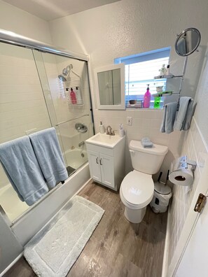 Un baño con ducha envuelta en vidrio, un lavabo blanco, un inodoro y una ventana pequeña.