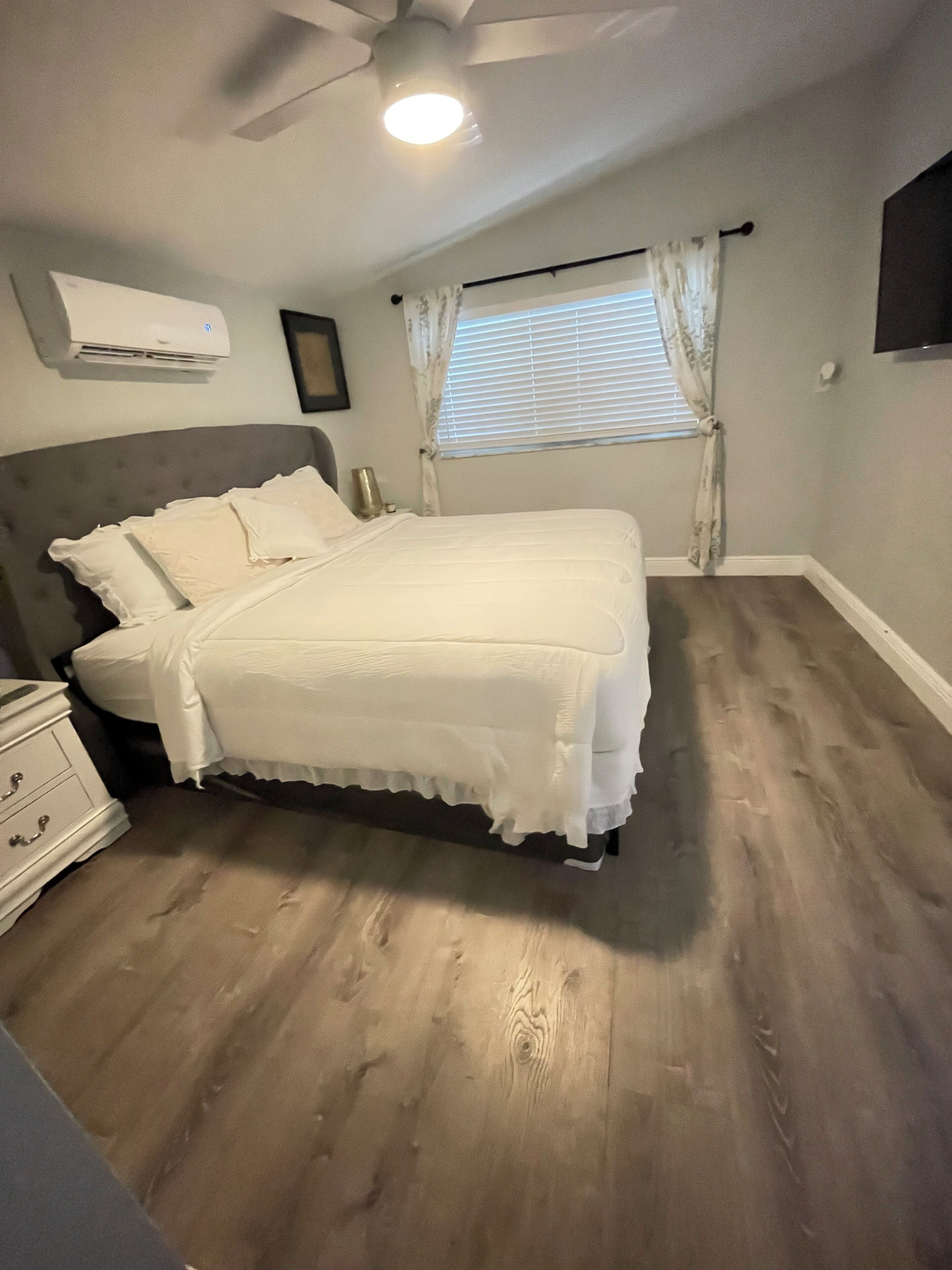 A bedroom with a bed, a nightstand, a dresser, a ceiling fan, and a window with curtains.