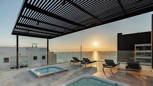 Een dakterras met een zwembad, lounge fauteuils en uitzicht op de ondergaande zon boven de oceaan.