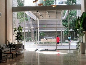 A modern lobby with a glass entrance, a sofa, a coffee table, and potted plants.
