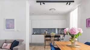 A modern kitchen with white cabinets, a wooden dining table, and a vase of flowers.