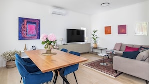 A modern living room with a wooden dining table, blue chairs, a grey sofa, and a flat-screen TV.