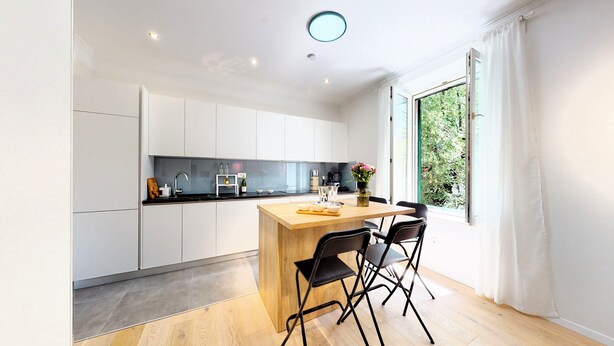 A modern kitchen with white cabinets, a wooden island, and a large window with a view of greenery.