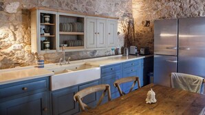 A rustic kitchen with stone walls, a wooden table, and a stainless steel refrigerator. - Luxury Villa in Zavala w/pool (Zavala, Jelsa)