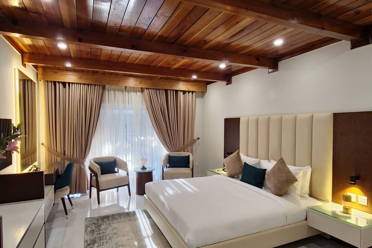 Une chambre d’hôtel moderne, dotée d’un grand lit, de deux tables de chevet, d’un bureau, d’une chaise et d’une grande fenêtre avec des rideaux.