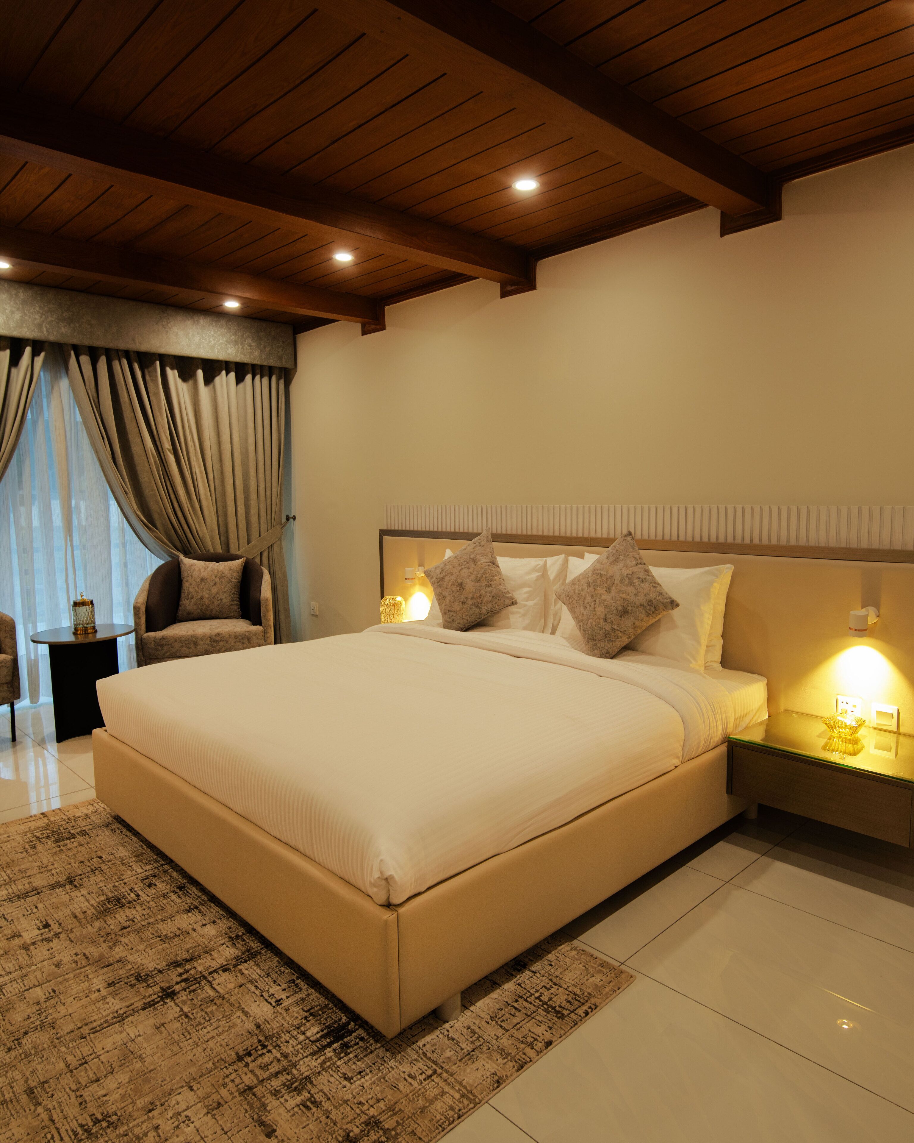 A bedroom with a large bed, a nightstand with a lamp, and a chair.