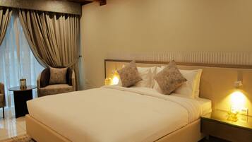 A bedroom with a large bed, a nightstand with a lamp, and a chair.