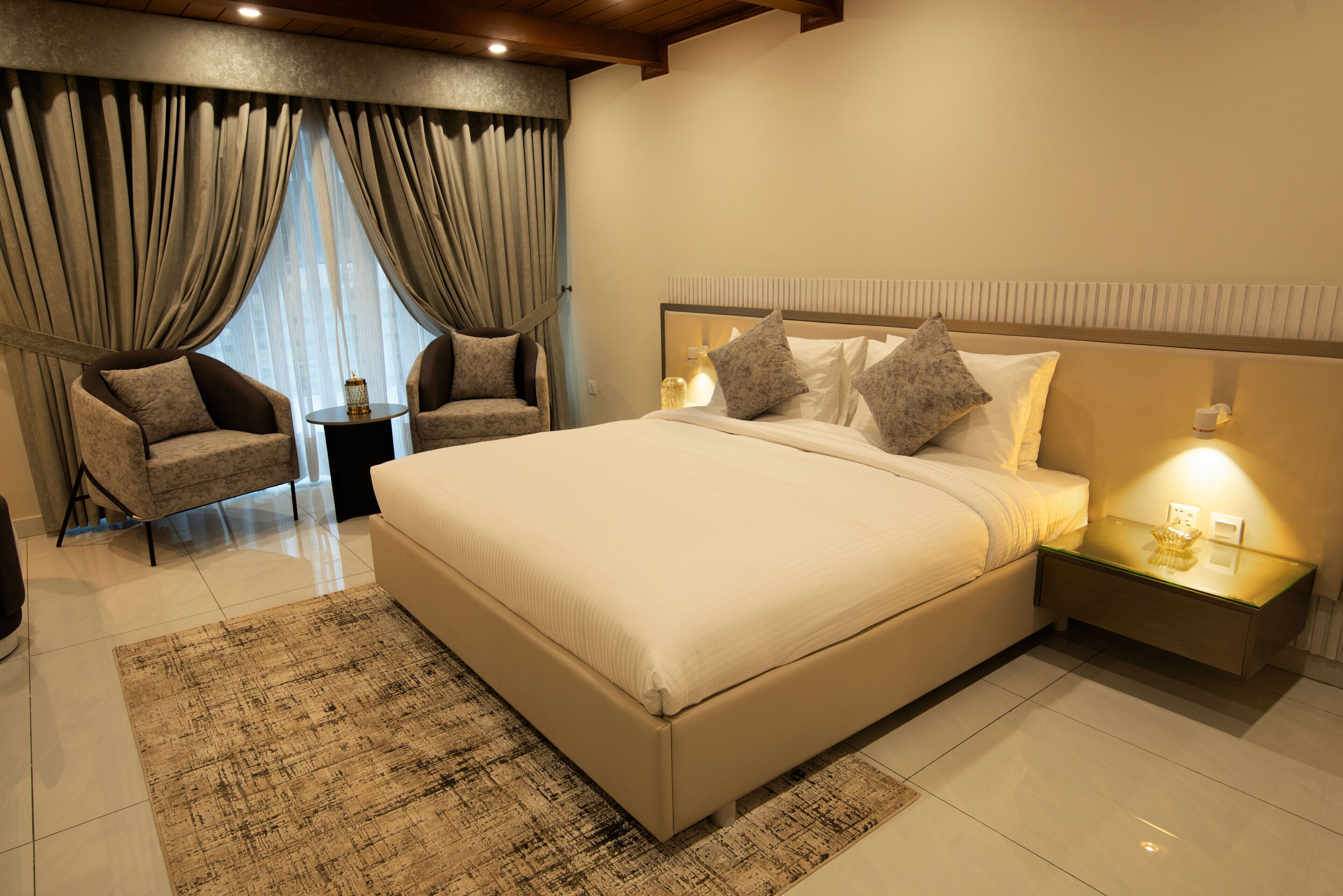 A bedroom with a large bed, two bedside tables, a nightstand, a chair, and a window with curtains.