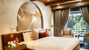 Une chambre spacieuse avec un grand lit, un plafond en bois et une vue sur l’extérieur grâce à de grandes fenêtres.