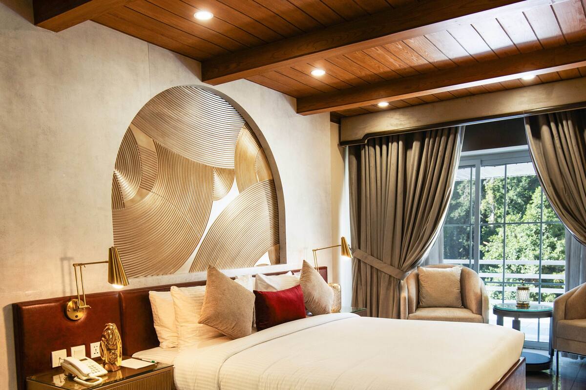 Une chambre spacieuse avec un grand lit, un plafond en bois et une vue sur l’extérieur grâce à de grandes fenêtres.