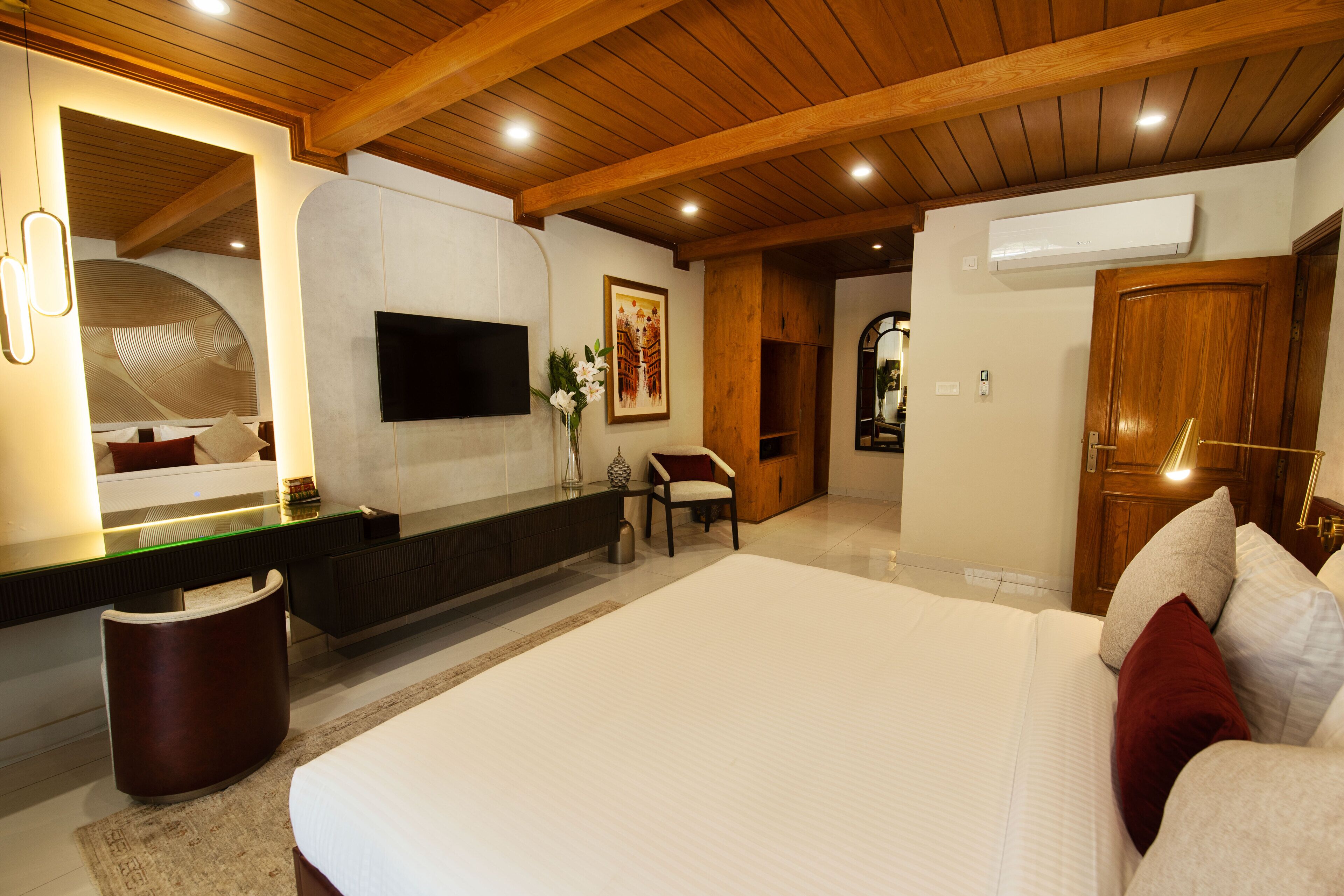 A modern bedroom with a large bed, a flat-screen TV, a wooden ceiling, and a built-in bench.
