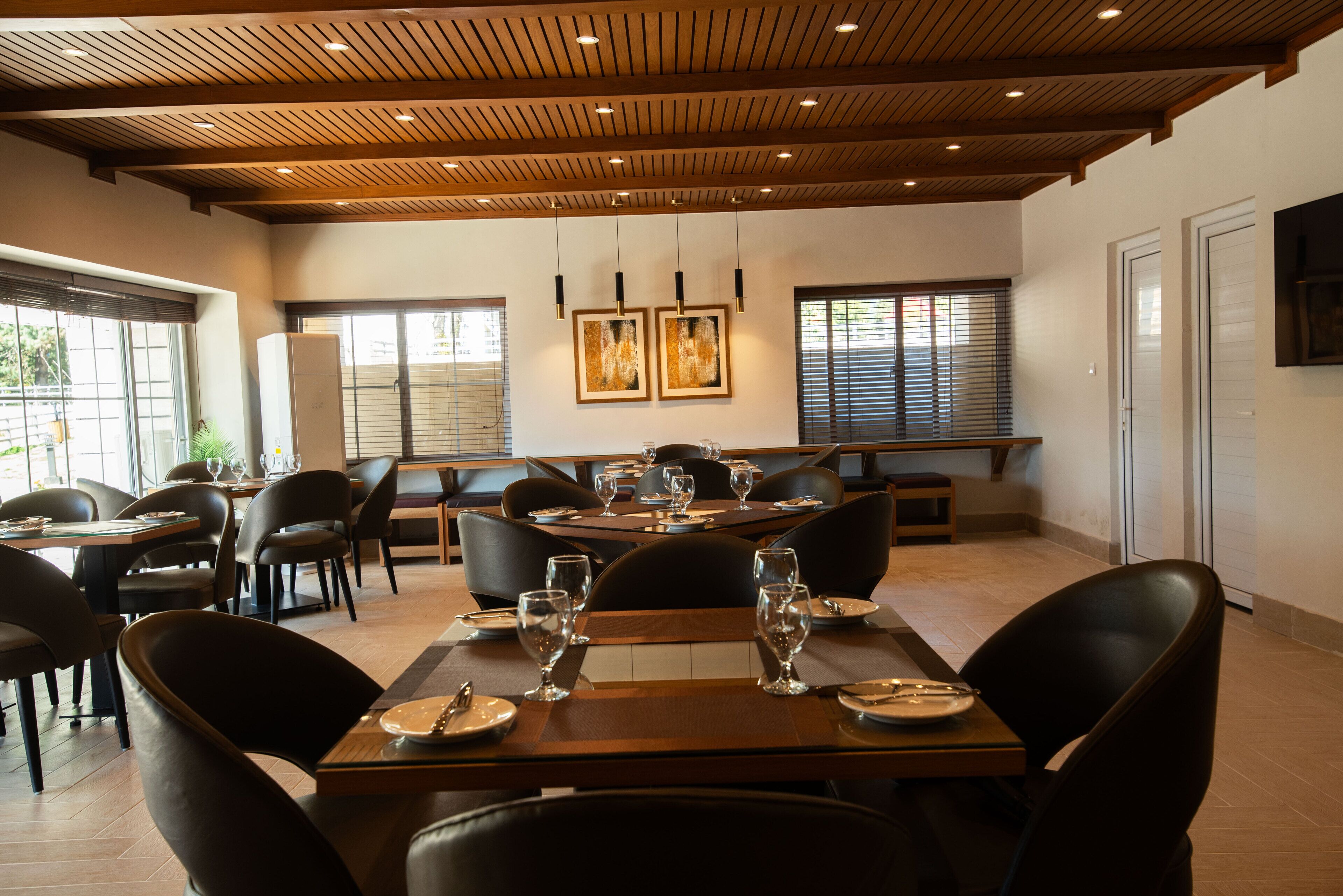 Un restaurante con vigas de madera en el techo, sillas de cuero negro y mesas dispuestas para comer.