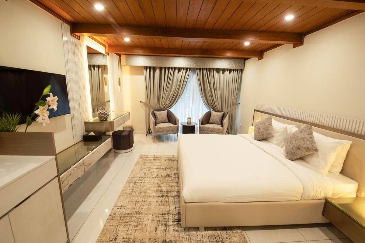 Une chambre moderne avec un grand lit, deux fauteuils, une petite table et un téléviseur.