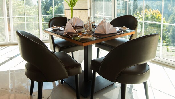 Un coin repas avec une table dressée pour quatre personnes, entouré de chaises, de grandes fenêtres et offrant une vue sur un paysage montagneux.