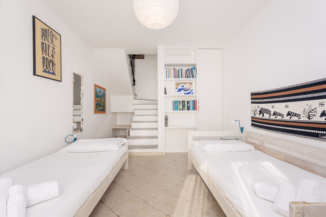 A hotel room with two single beds, a bookshelf, a staircase, and a wall tapestry.