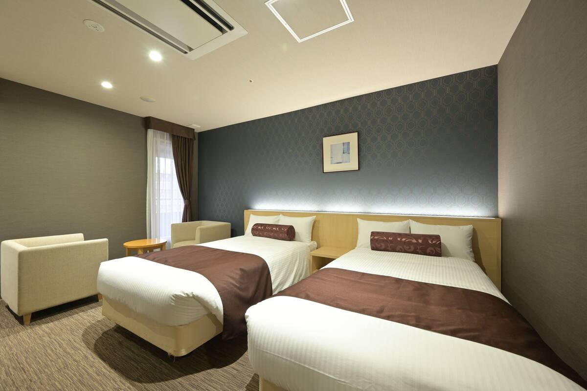 A hotel room with two beds, a sofa, a small table, and a window with curtains.
