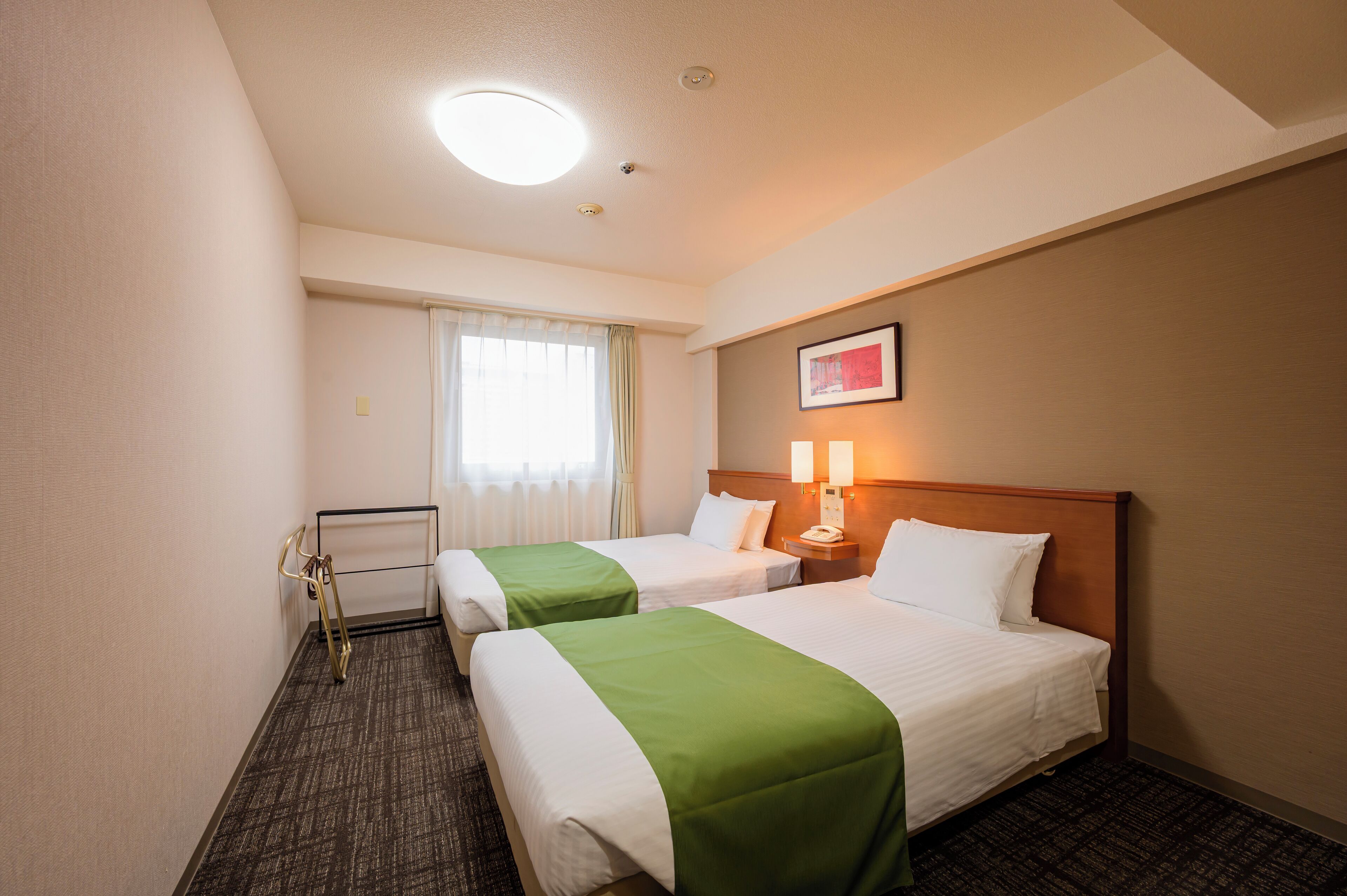 Habitación de hotel con dos camas, un escritorio y una ventana con cortinas.