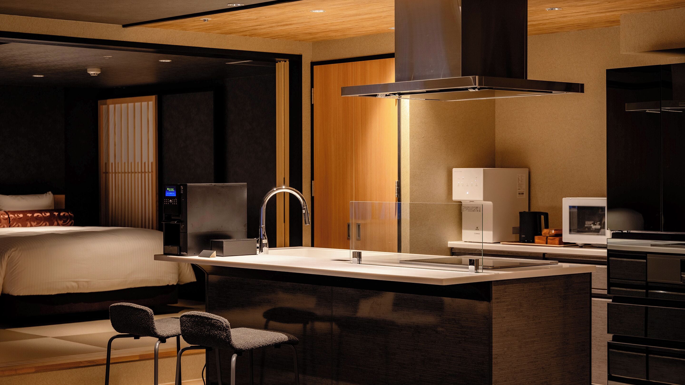 A modern hotel room with a bed, a desk with a sink, a coffee maker, and a television.