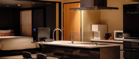 A modern hotel room with a bed, a desk with a sink, a coffee maker, and a television.