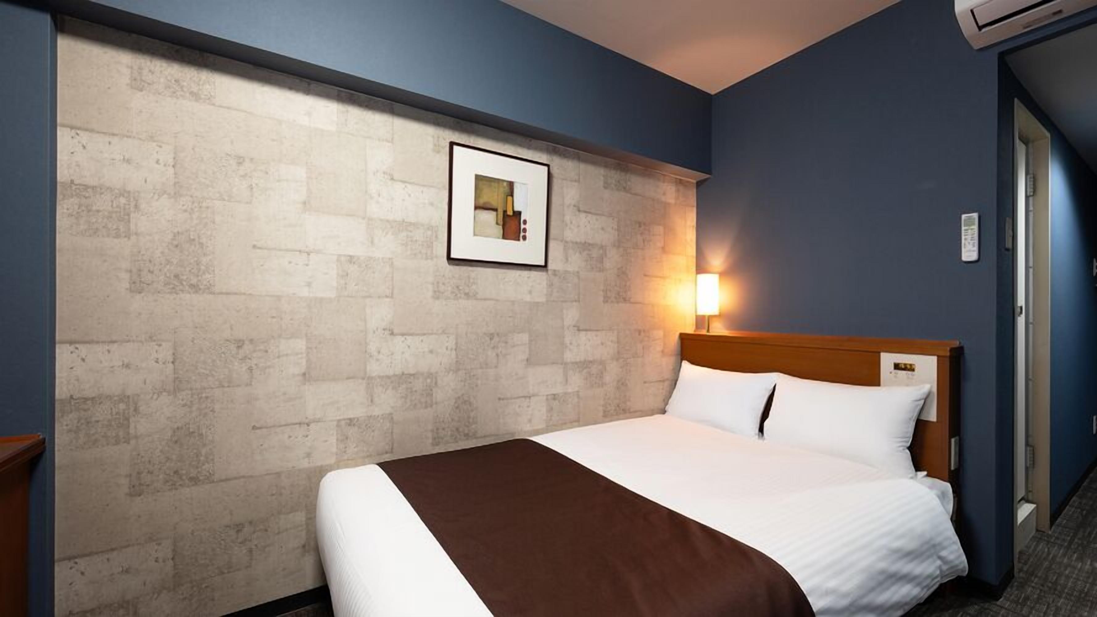 A hotel room with a bed, a wall-mounted picture, and a nightstand.
