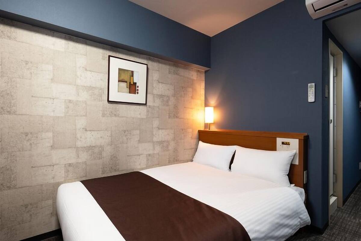 A hotel room with a bed, a wall-mounted picture, and a nightstand.