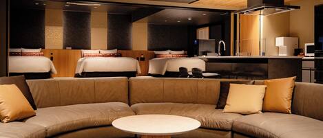 A hotel room with a curved sofa, a round table, and two beds with headboards.