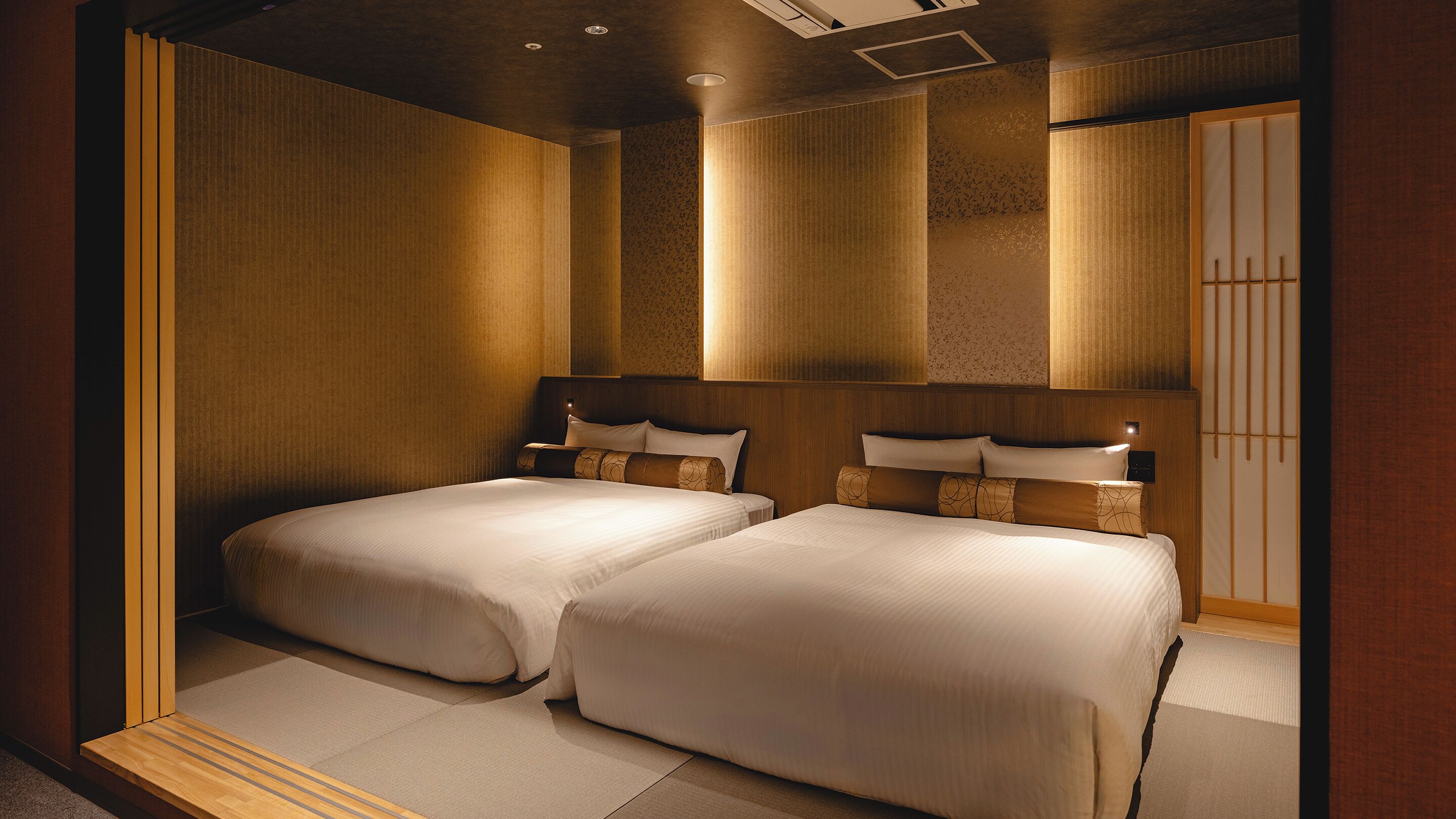 A hotel room with two beds, wooden headboards, and a traditional Japanese-style sliding door.