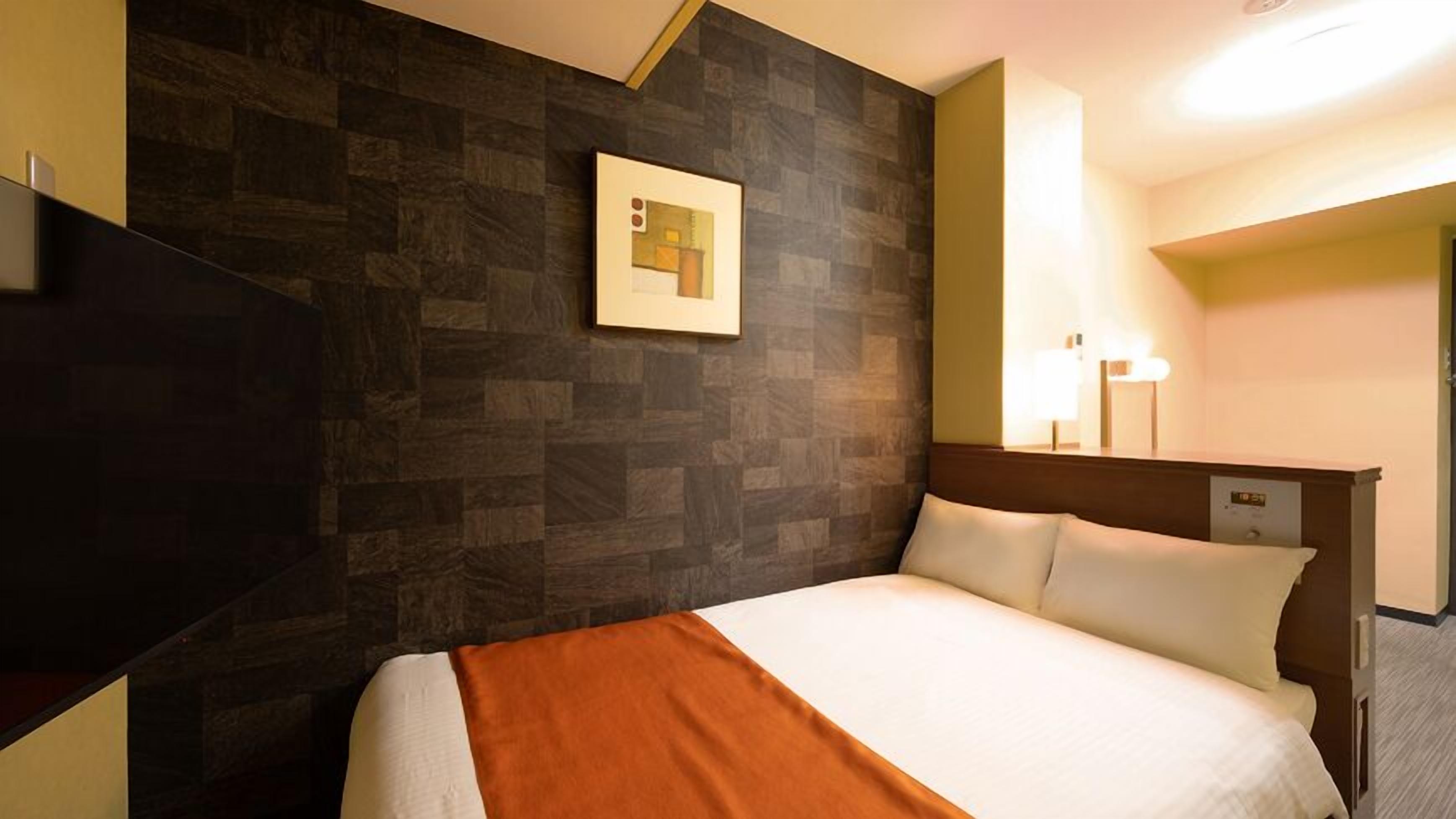 A hotel room with a bed, a nightstand, a wall-mounted TV, a framed picture, and a bedside lamp.
