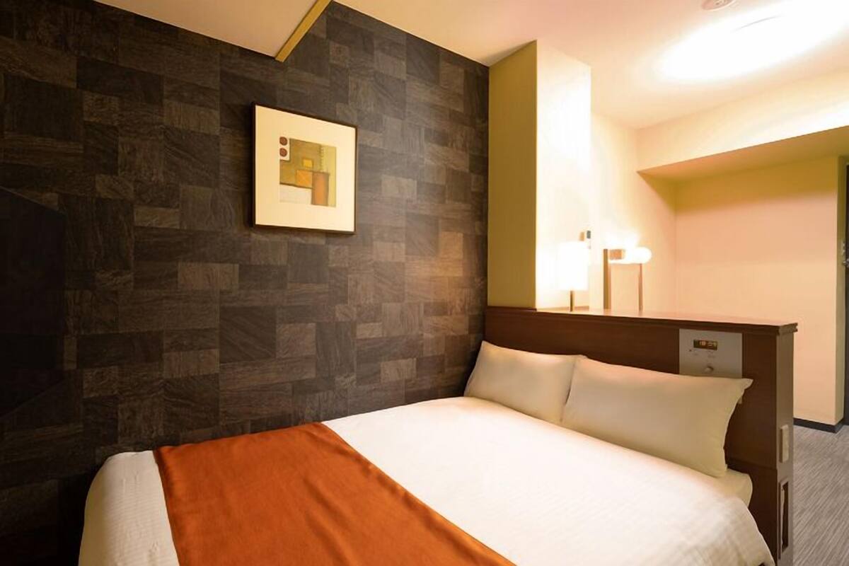 A hotel room with a bed, a nightstand, a wall-mounted TV, a framed picture, and a bedside lamp.