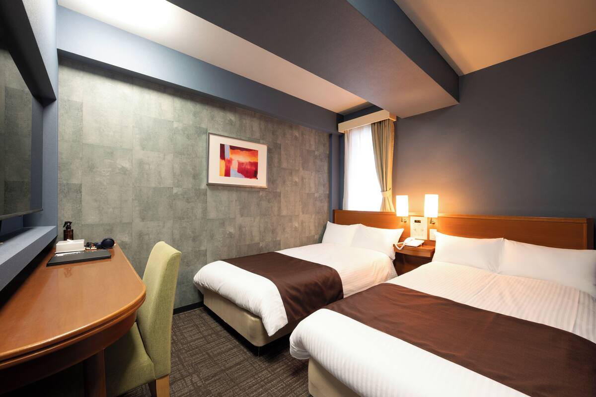A hotel room with two beds, a desk, a chair, a television, and a framed picture on the wall.