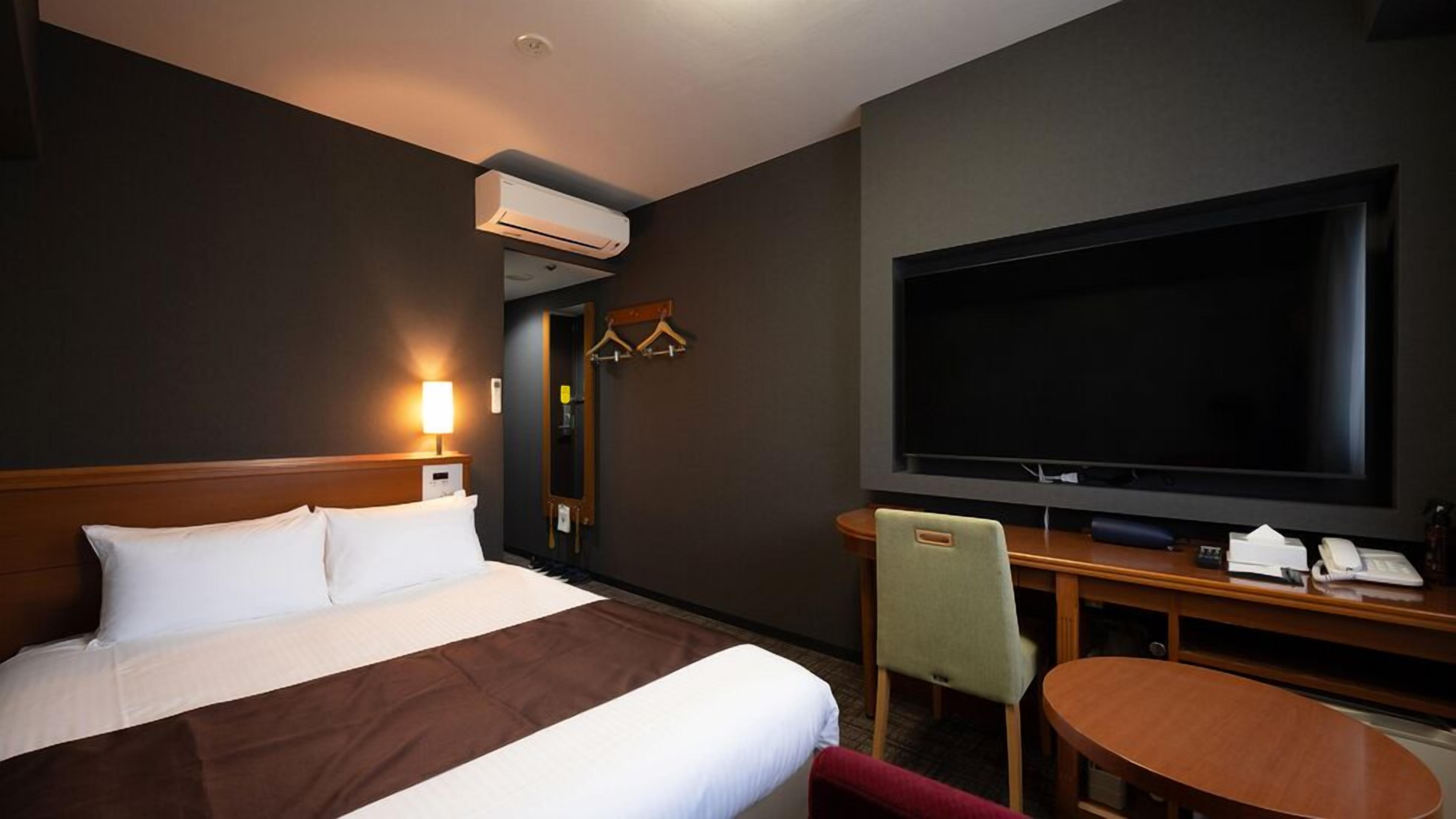 A hotel room with a bed, a TV, a desk with a chair, and a small table.