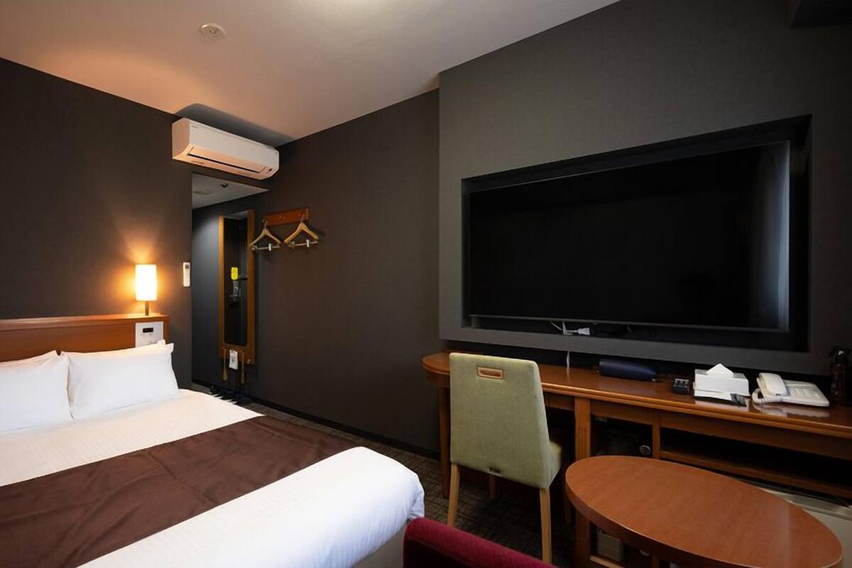 A hotel room with a bed, a TV, a desk with a chair, and a small table.