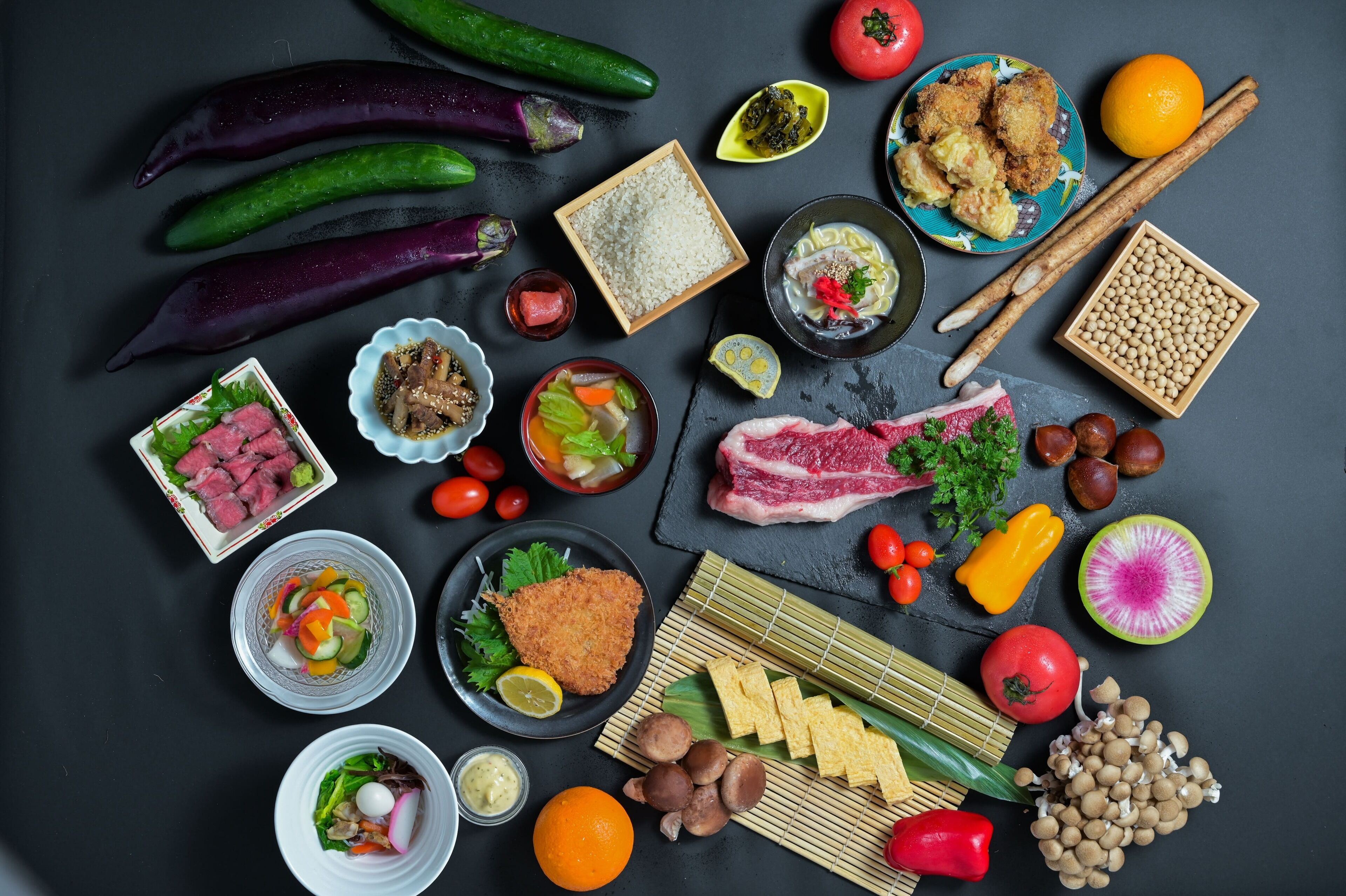 A variety of food items including vegetables, meat, and tofu arranged on a dark surface.