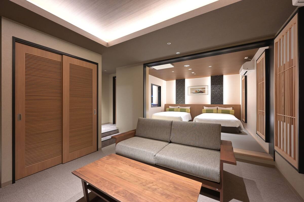 A hotel room with a sofa, a wooden table, and a bed with two pillows.