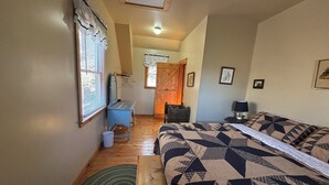 A bedroom with a large bed, a desk, a chair, a small table, a lamp, and a window with blinds. - Rooster's Perch Cabin at Country Manor Acres in Townsend, TN (Townsend)