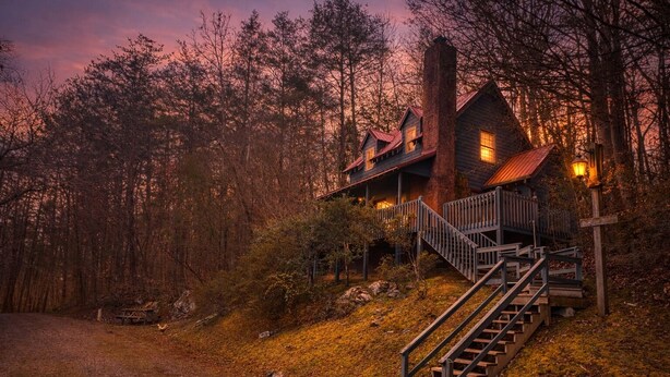 A rustic cabin with a staircase leading to a porch, surrounded by a forest. - Rooster's Perch Cabin at Country Manor Acres in Townsend, TN (Townsend)