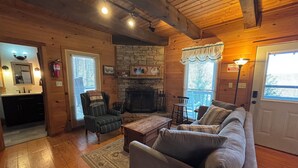 A cozy cabin interior with a stone fireplace, wooden walls, a sofa, and a dining table. - Rooster's Perch Cabin at Country Manor Acres in Townsend, TN (Townsend)