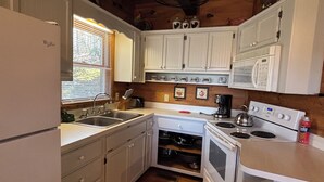 A compact kitchen with white cabinets, a built-in oven, a microwave, and a sink. - Rooster's Perch Cabin at Country Manor Acres in Townsend, TN (Townsend)