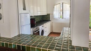 A compact kitchen with white cabinets, a tiled backsplash, a built-in oven, a washing machine, and a window with curtains. - Maison de pêcheur with Air-conditioned and mooring, Wi-Fi, for 7 persons, near the beach (PORT GRIMAUD)
