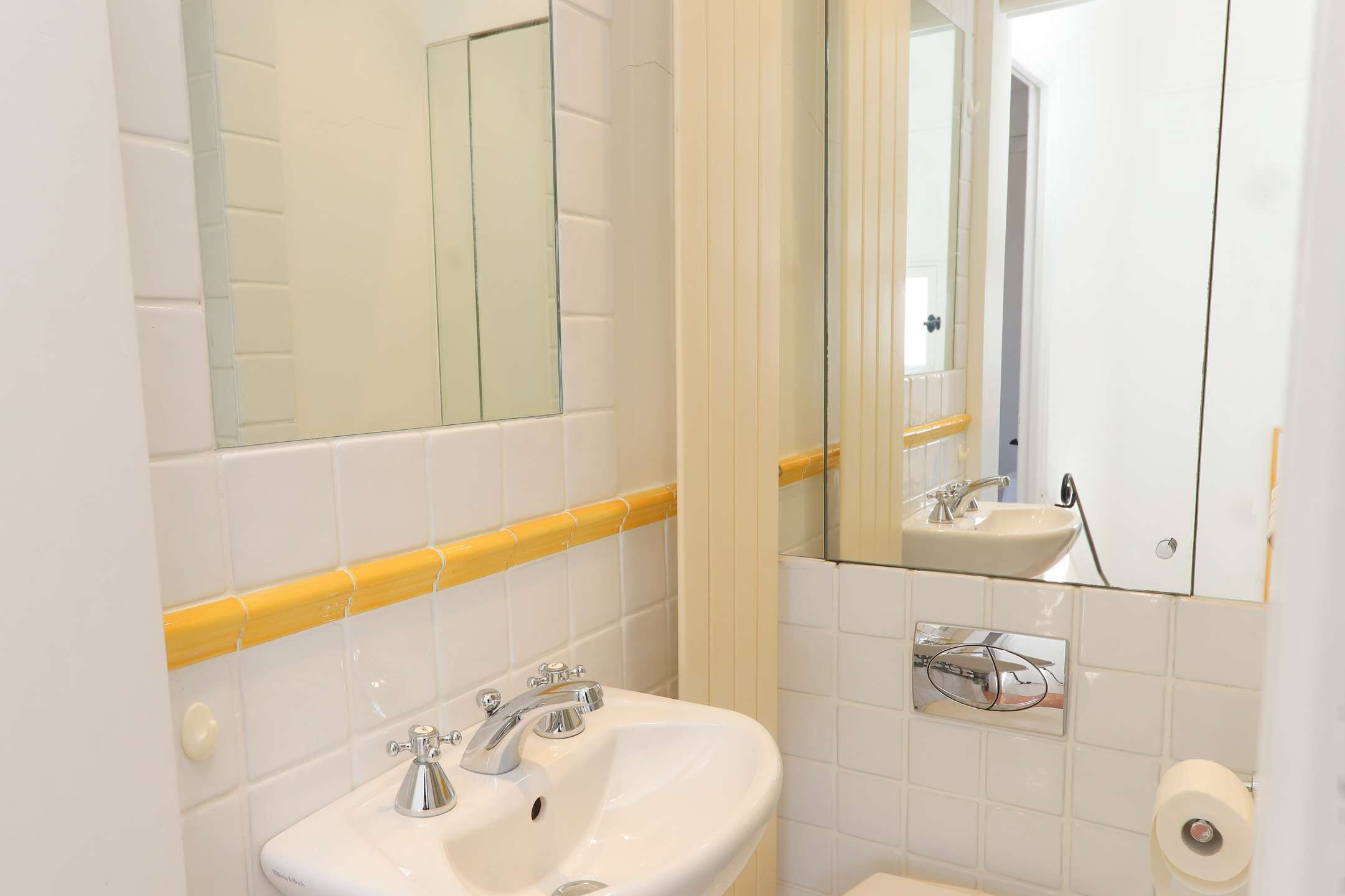 A bathroom with a white sink, two faucets, a mirror, and a toilet.
