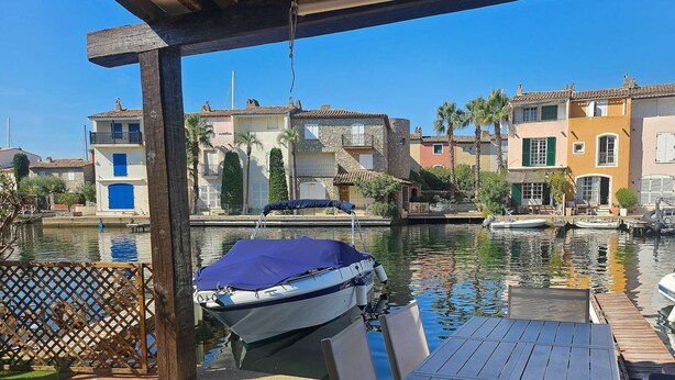 A marina with boats docked, a covered seating area with tables and chairs, and a backdrop of colorful buildings along the water. - Maison de pêcheur with Air-conditioned and mooring, Wi-Fi, for 7 persons, near the beach (PORT GRIMAUD)