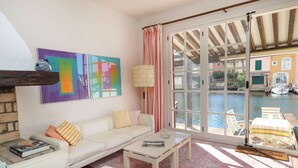 A cozy living room with a white sofa, a coffee table, and a view of a canal through large glass doors. - Maison de pêcheur with Air-conditioned and mooring, Wi-Fi, for 7 persons, near the beach (PORT GRIMAUD)
