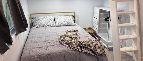 A bunk bed with a grey quilt, a patterned throw blanket, and a white headboard.