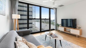 A modern living room with a sofa, TV, and large windows overlooking a cityscape. - Centre of Brisbane at RiverFront (Brisbane City)