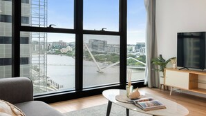 A modern living room with a large window, a sofa, a coffee table with a book, a TV, and a desk. - Centre of Brisbane at RiverFront (Brisbane City)
